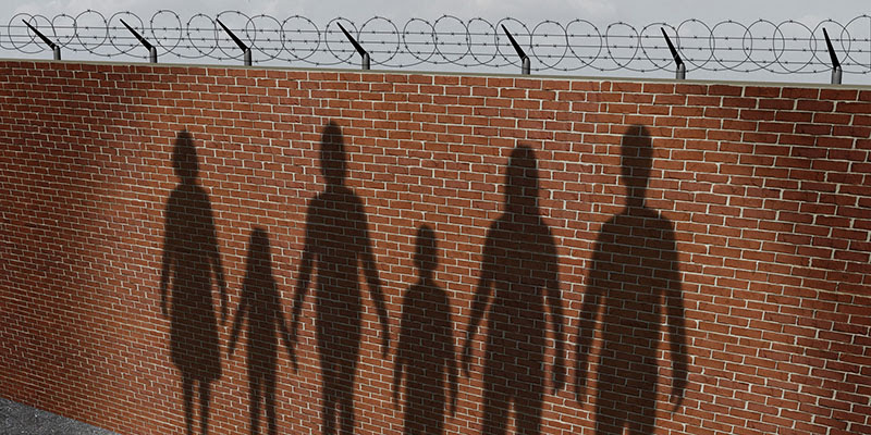 Shadows of a family cast against a brick wall with barbed wire